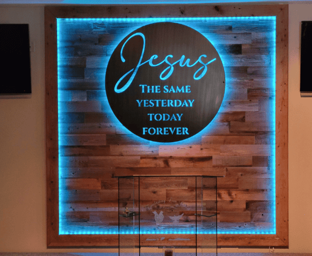 Wood panel with words 'Jesus the same yesterday today forever' carved into it backlit by blue LED light.
